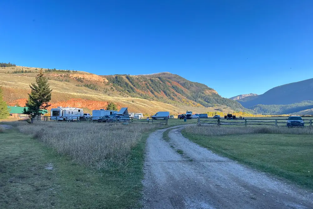 A dirt road in a field with mountains in the background and a camping area nearby