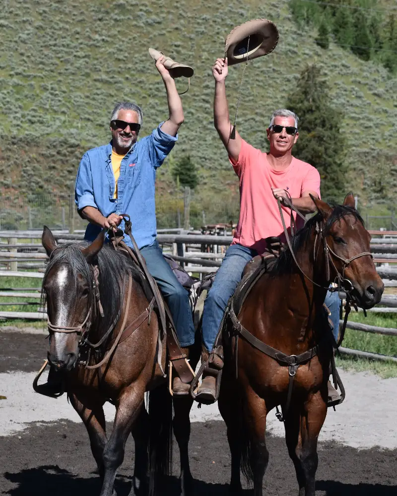 Two men riding horses and raising their hats