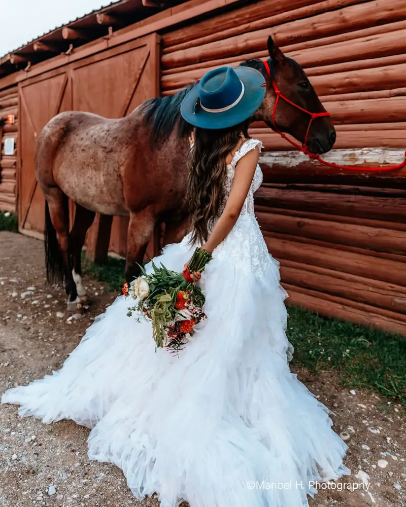 A woman in a white dress holding flowers next to a horse