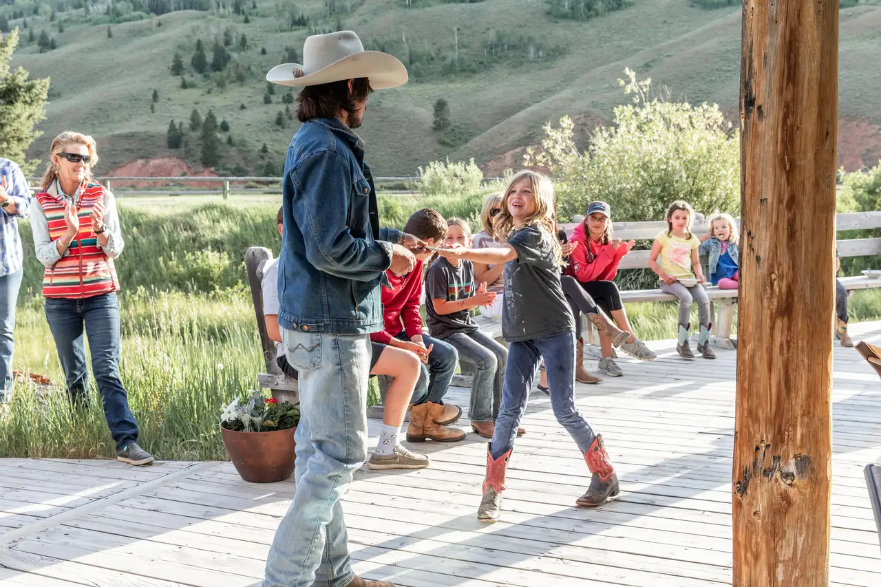 A man and a girl dancing on a wooden deck, with a group of children and adults watching