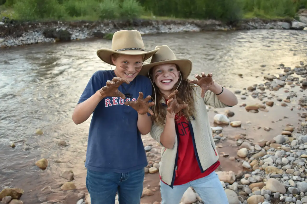 Two kids posing with their hands up and wearing cowboy hats