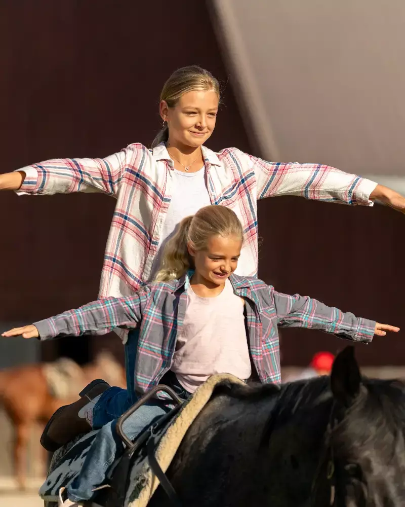 A woman and a young girl are riding a horse together and enjoying the moment