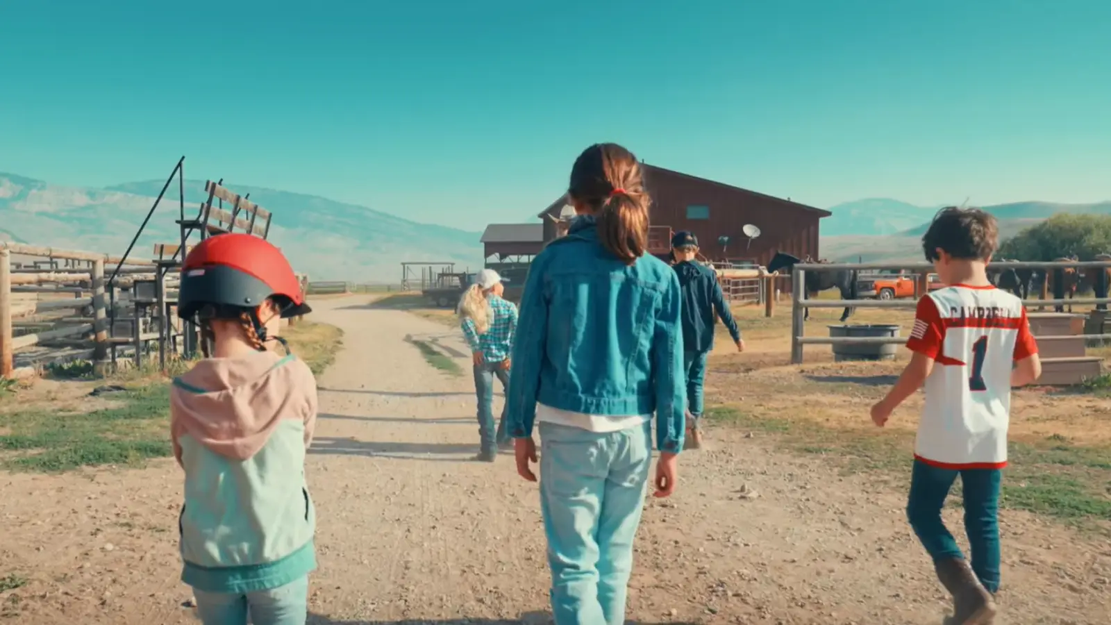 A group of people walking down a dirt road, with a young girl in a red helmet leading the way