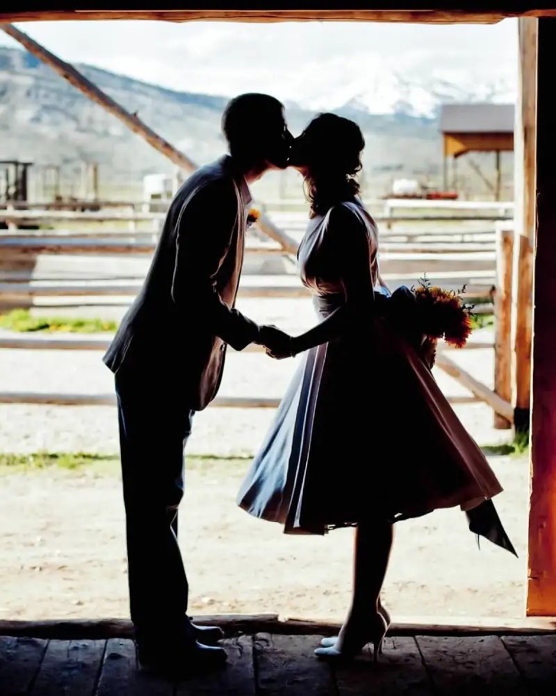 A couple kissing in front of a fence and a building