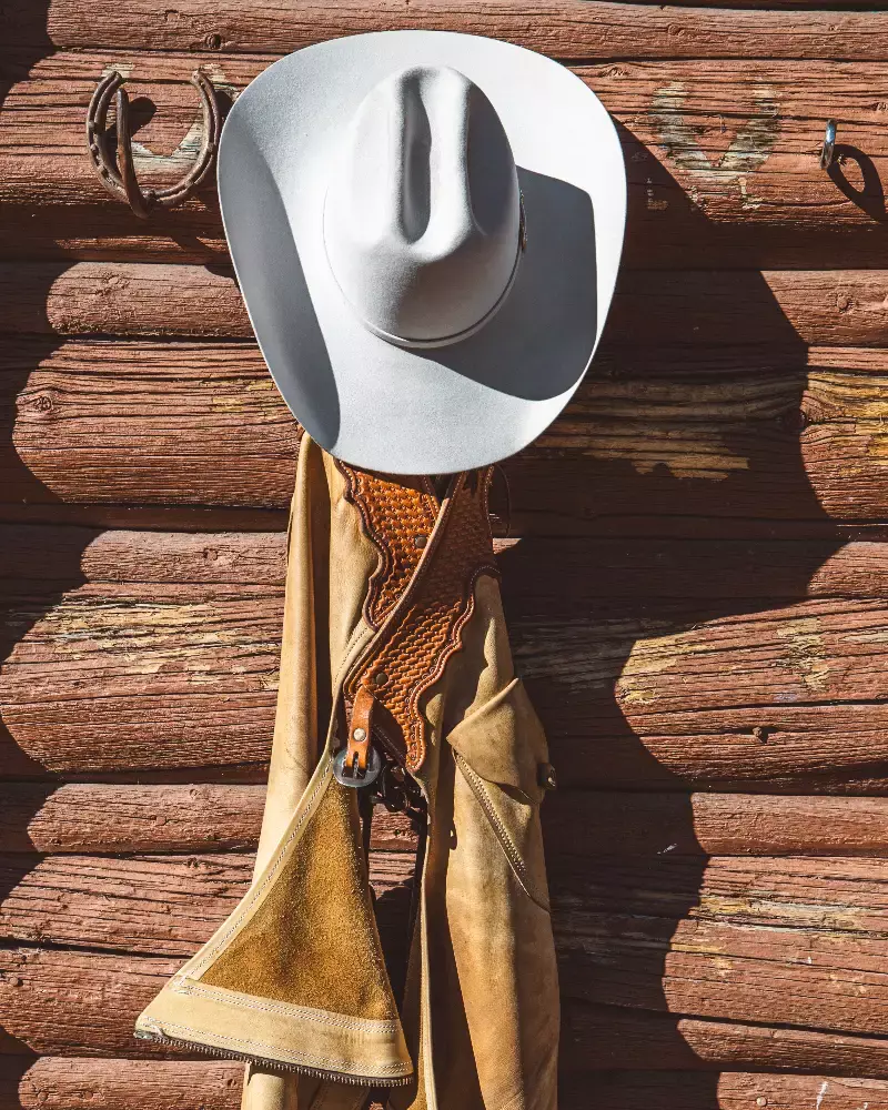 A white cowboy hat hanging on a wall with a brown jacket and a lasso underneath it