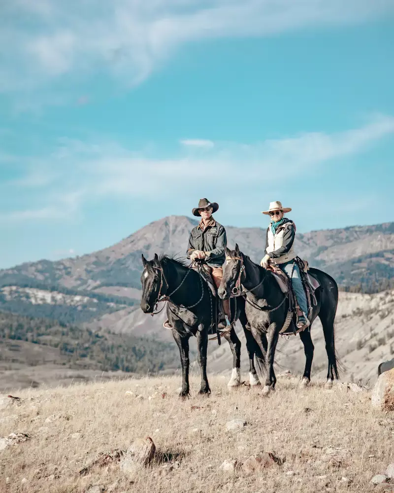 Two men on horses on a hillside with a mountain in the background