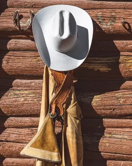 A white cowboy hat hanging on a wall with a brown jacket and a lasso underneath it