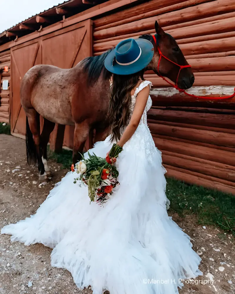 A woman in a white dress holding flowers next to a horse